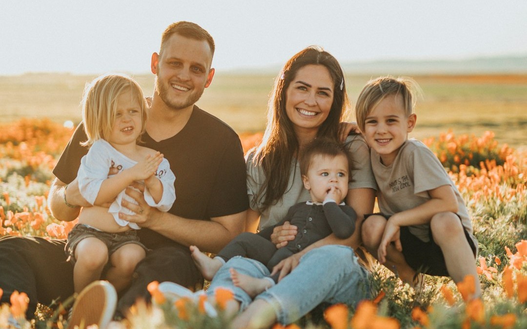 3 women and 2 men sitting on green grass field during daytime